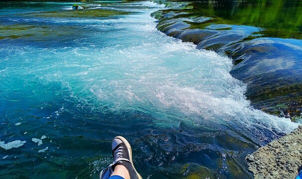 Woman with blue sneakers  sitting by the green river with waterfalls in magnificent green nature