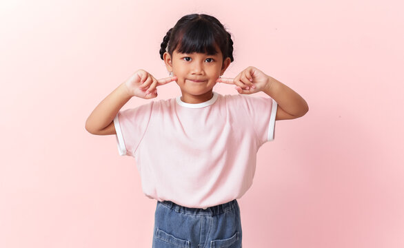Adorable young Asian girl pointing fingers at her cheeks. Portrait of cute Asian child with sweet expression and dimples on pink background.