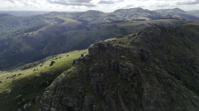 Drone lowers in medium wide shot of east side of Sheba's Breast mountain peak on partially cloudy day in Ezulwini Valley, Eswatini