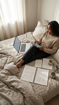 Young woman studying on bed with laptop and notebook, soft morning light through curtains, calm focused mood for home learning and productivity