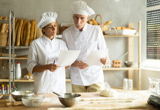 Two experienced bakers read new recipe on paper, discussing a method for making delicious bread