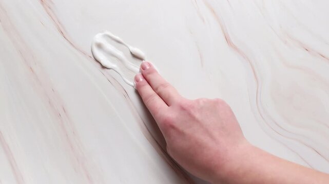 Woman hand spreading cosmetic cream on surface, skincare texture demonstration with lotion smear