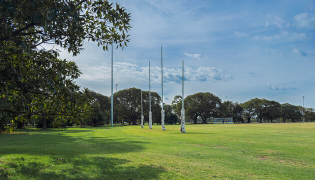 The iconic white AFL goal posts stand tall at Ikon Park (Princes Park) in Carlton, Melbourne, set against a backdrop of lush green turf on a bright, clear afternoon.