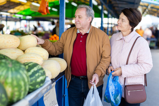 elderly man and woman buy a melon at an open market