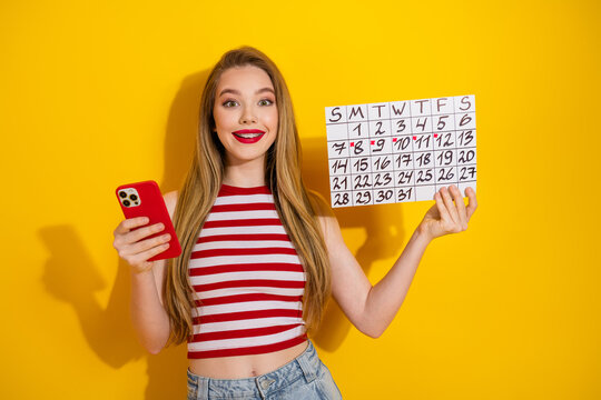 Happy young woman holding a calendar and smartphone against bright yellow background promoting lifestyle and planning