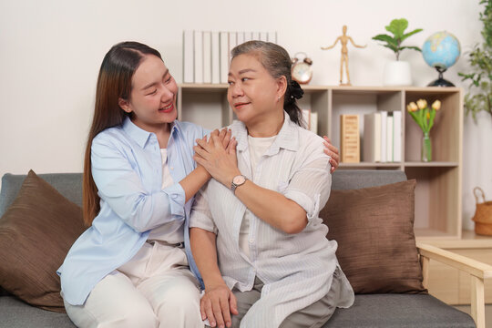 Asian daughter caring for senior mother, showing support at home living room