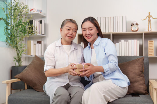 Asian mother and daughter giving gift, celebrating family in home living room