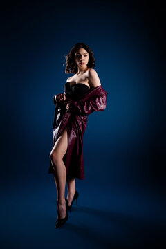 Fashion model in a burgundy leather coat and black bustier posing confidently in studio lighting, high heels and dramatic pose conveying glamour and elegance