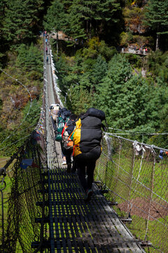 Nepalian Porter carrying heavy load on his back going along the bridge to Everest Base camp. Himalayas. Nepal.