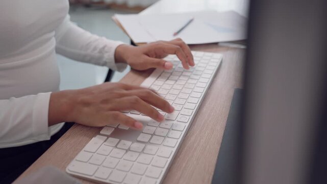 Close up view of woman typing on white keyboard at office desk with paperwork. Concept of office task execution, clerical duties, documentation, and everyday business operations.