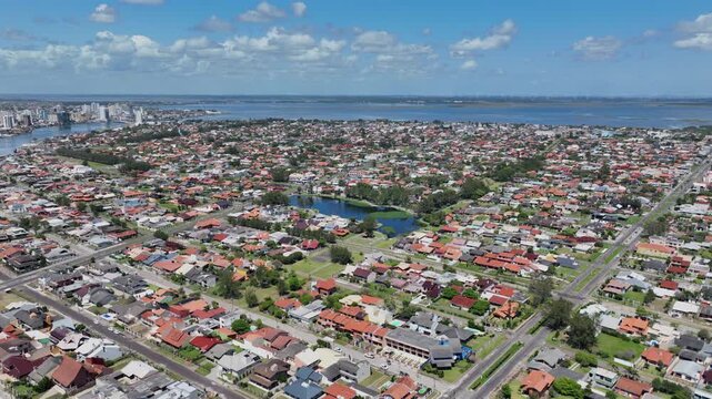 Aerial approach to Lago do Braco Morto in central Imbe, with surrounding neighborhoods, Rio Tramandai and distant Tramandai skyline.