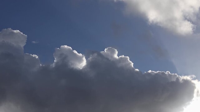 Upward view of clouds with silver lining passing before sun in blue sky
