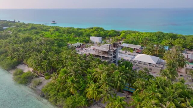 Aerial drone footage showing a large multi story apartment building under construction near the coastline of Vashafaru Island, contrasting with the traditional tropical island skyline in northern Mald