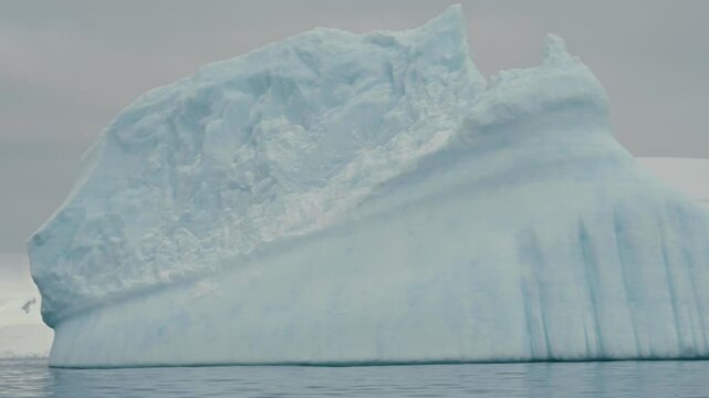 Extreme close-up pass alongside massive pale blue Antarctic icebergs revealing contrasting smooth striated and eroded textured surfaces