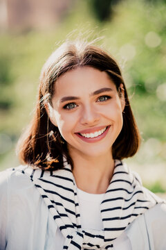 Smiling young woman portrait outdoors in natural light wearing a striped sweater, casual fashion headshot conveying happiness, confidence and approachable beauty