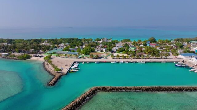 Smooth aerial drone footage flying parallel along the harbor and coastline of Vashafaru Island with boats, tropical shoreline and turquoise waters in northern Maldives.