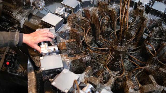 A complex industrial machine with multiple hydraulic lines processing metal components in a manufacturing plant environment with shavings.