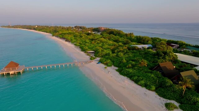 Smooth aerial drone flyover of the long beach jetty in Vashafaru Island, surrounded by crystal clear turquoise water and white tropical shoreline in northern Maldives.
