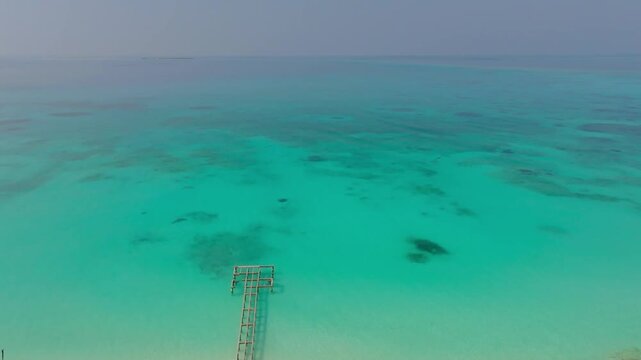 Beautiful reverse aerial drone footage flying over an old damaged jetty, then across Vashafaru Island with simple homes, palm trees, white sandy beaches and turquoise waters in northern Maldives.