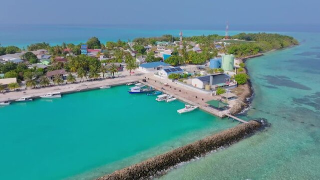 Cinematic drone dronie shot revealing the harbor of Vashafaru Island with tropical coastline, boats and turquoise waters in northern Maldives.