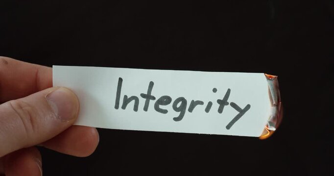 Hand burning a paper labeled &ldquo;Integrity,&rdquo; symbolizing loss of values, ethical conflict, and broken principles.
