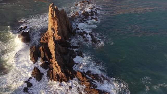 Majestic aerial view of the wild Cabo de Gata coastline. Turquoise ocean waves crashing against the Sirens Reef rock formations at sunset