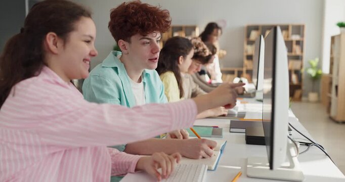 Students teenagers study collaboration in classroom computer lab. Focused peers share ideas at screens and take notes while learning with teacher guidance. Clear concept of education teamwork.