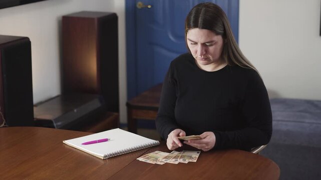 Concerned woman counts cash at a table at home, checking bills and realizing there is not enough money for expenses, budgeting or financial stress.