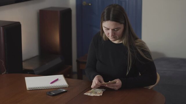 Focused woman counts cash at a table and ignores a ringing phone, useful for finance, budgeting, debt, or distraction concepts.