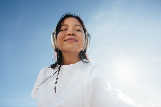 Woman listening with headphones outdoors, feeling relaxed