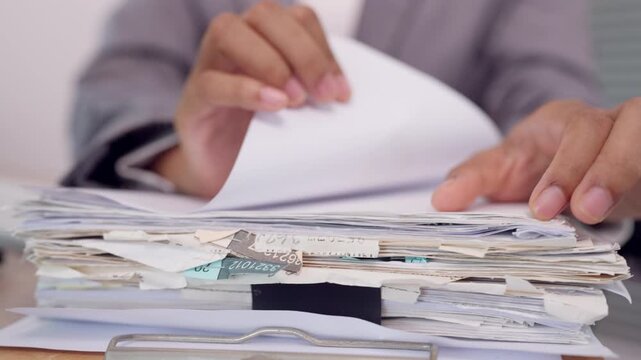 Close up of businesswoman clipping stack of documents with binder clip on clipboard at office desk. Concept of document organization, paperwork preparation, and office filing workflow.