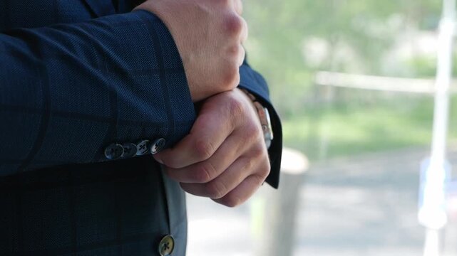Close-up of the groom in a black jacket adjusting cufflinks and shirts. The groom gets dressed in the morning.