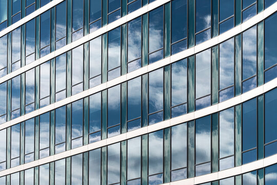 Modern curved glass building architecture facade with sky reflection and abstract pattern creating a sleek urban background with flowing lines