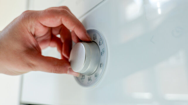 Close-up of a hand turning a dial on a white appliance with various symbols
