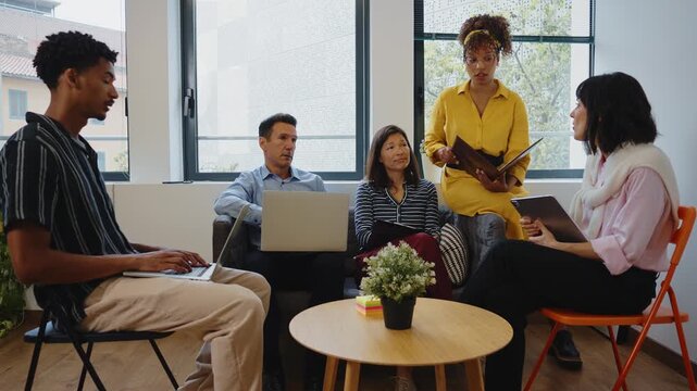 Multiethnic group of professionals attentively listening to a speaker during a collaborative meeting in a modern office, fostering teamwork, communication, and innovative business strategies