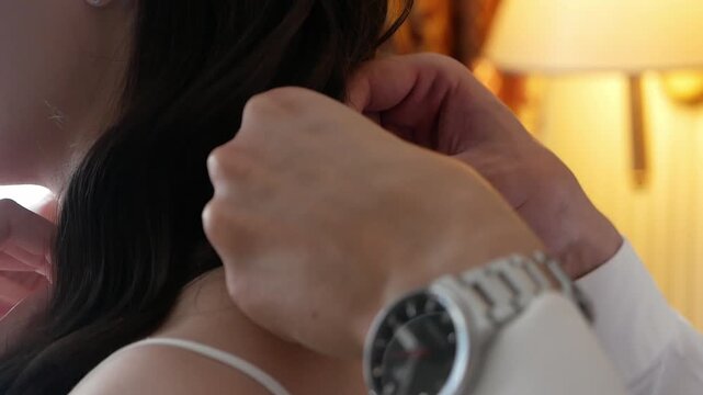 Close-up of a man fastening a necklace around a woman's neck. A man in love gives his girlfriend a necklace.