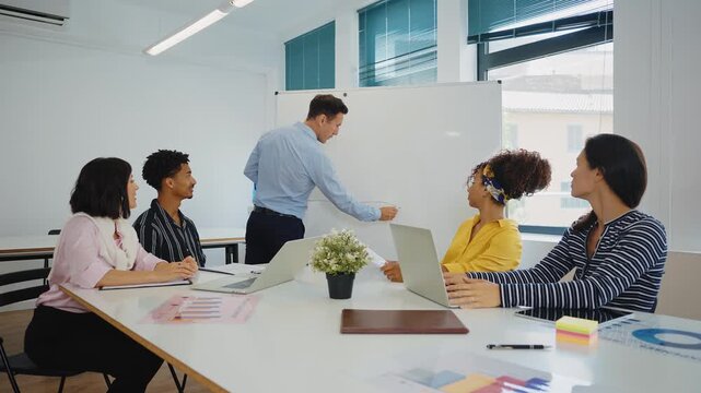 Multicultural business people brainstorming and talking about a new project during a briefing, analyzing data and charts on papers and laptops in a bright and modern conference room