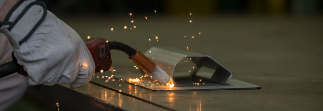 製造業の工場で火花散るアーク溶接の金属加工の手元のクローズアップ工業技術背景素材　オレンジの光