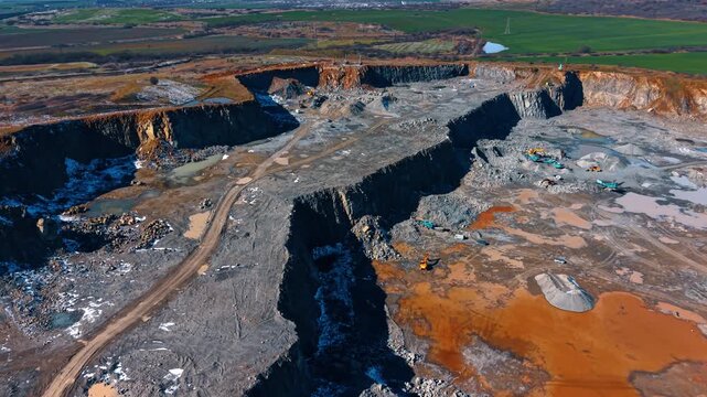 Wide panorama of open pit stone quarry with heavy machinery. Aerial shot of active limestone quarry with excavators and industrial trucks in a landscape