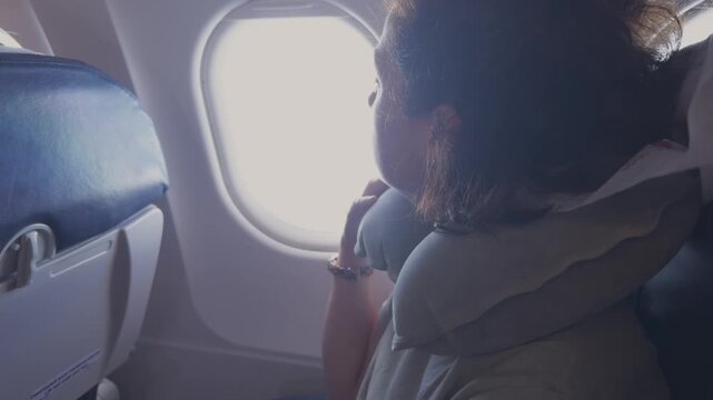 Passenger woman is flying in plane. Girl sitting in airplane looking out window going on trip vacation travel. Traveling female inside plane enjoying flight. Traveling girl