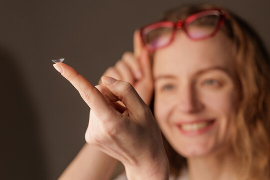 Woman holding contact lens on finger with glasses for vision correction