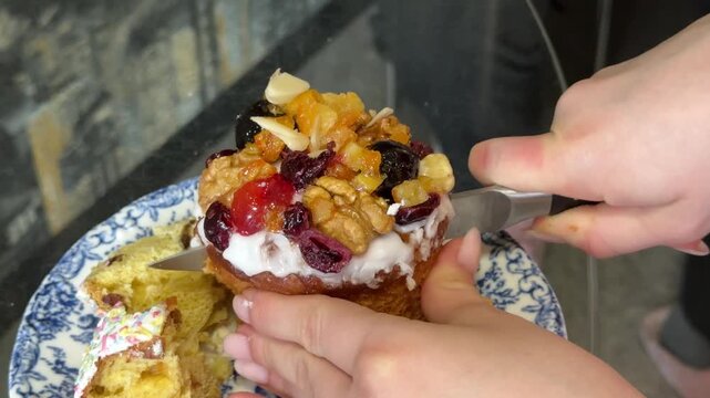 traditional panettone Easter bread being cut with a knife. The slice reveals dried fruits and caramelized nuts, with caramelized grapes on top, highlighting a festive dessert preparation.