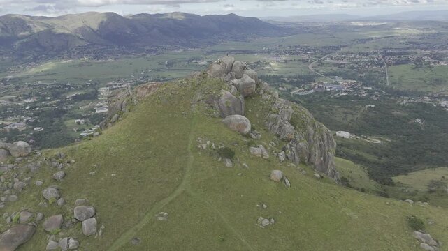 Drone facing west, flies up and away from Sheba's Breast peak overlooking valley on overcast afternoon in Ezulwini Valley, Eswatini