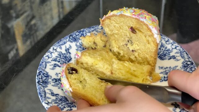 Close-up of a knife slicing traditional Easter bread served on a blue plate. The soft yellow dough with raisins reveals a tender texture, highlighting a fresh homemade baked dessert.