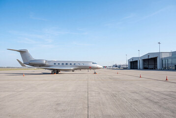 Fototapeta premium Silver private jet parked on airport apron near hangars in side view