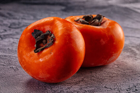 Two fresh ripe orange persimmons on a grey textured surface