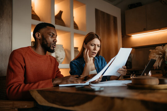 Interracial Couple Reviewing Bills and Financial Documents at Home with Concern and Stress