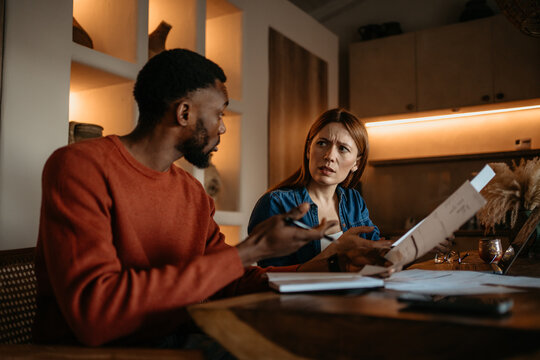 Interracial Couple Reviewing Bills and Financial Documents at Home with Concern and Stress