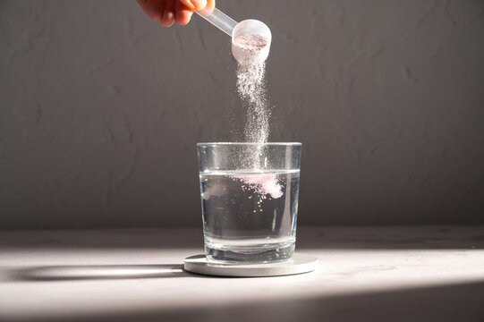 Pouring food supplement powder in glass of water. Collagen, protein powder, vitamins.