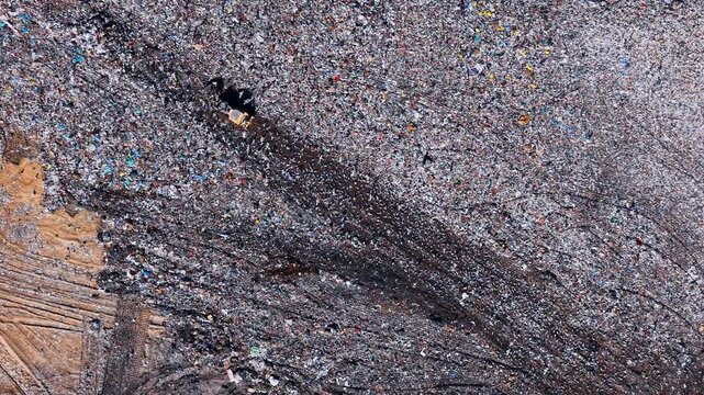 Landfill site has many waste layers. Workers manage a vast area filled with various types of waste at a landfill. Trash covers the ground and stretches far.
